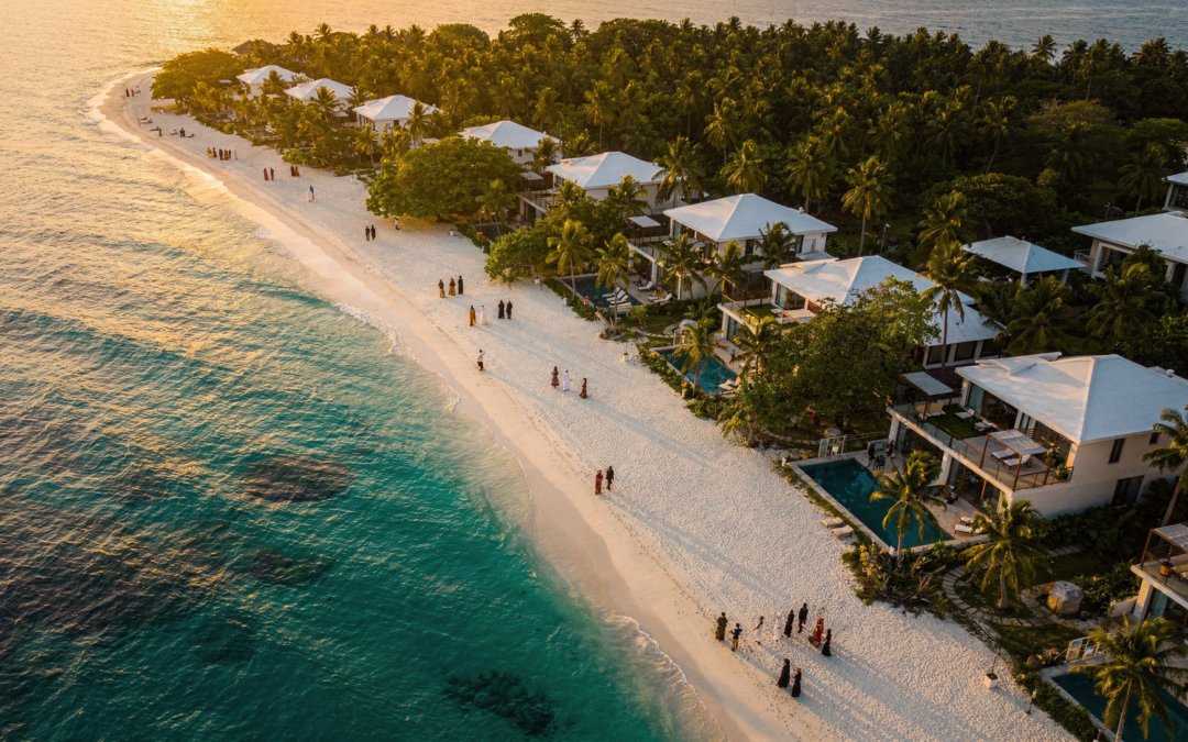 Aerial drone view of Zanzibar coastline with white sand beach, turquoise ocean, green palm trees, and luxury villas at golden hour.