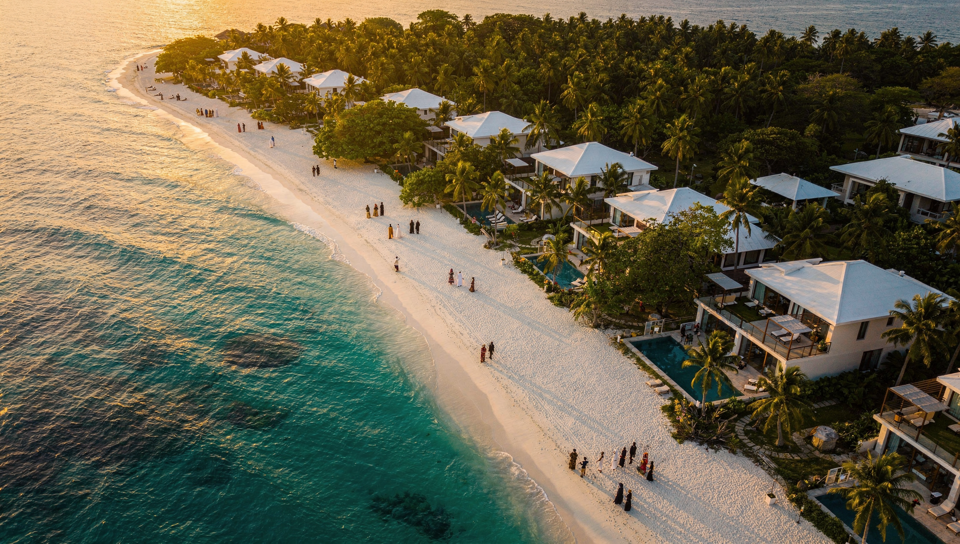 Aerial drone view of Zanzibar coastline with white sand beach, turquoise ocean, green palm trees, and luxury villas at golden hour.